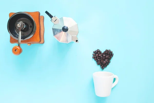 Pose plate créative de grains de café en forme de coeur et moulin à café et pot sur fond de couleur bleue — Photo