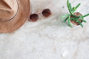 Yaratıcı düz moda güneş gözlüğü, hasır şapka ve beton arka planda çömlek kaktüs yatıyordu. Seyahat yaşam tarzı konsepti