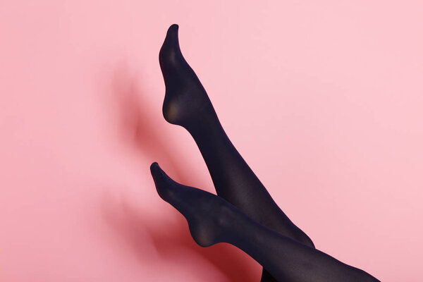 Legs of young caucasian woman in black tights on pink background