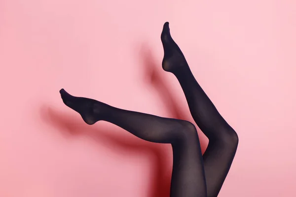 ピンク色の背景に黒タイツの若い白人女性の足 — ストック写真