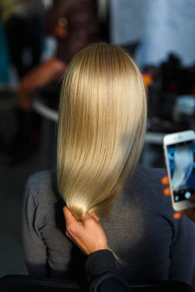 Hairdresser takes pictures on the smartphone result of hair coloring model. Rear view.
