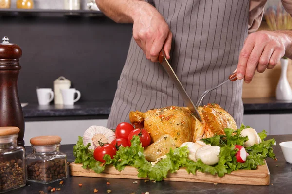 Las manos del jefe hombre cortando pollo al horno con verduras — Foto de Stock