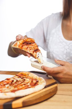 Bir kız yemeden önce bir dilim pizzayı plastik bir kaba bandırıyor.