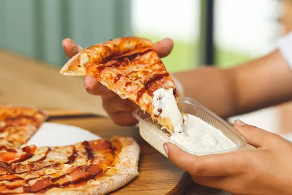 A girl dips a slice of pizza in sauce in a plastic container before eating it