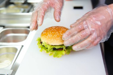 Şefin elleri bitmiş Burger 'ı gösteriyor. Restoranda hamburger hazırlıyorum. Aşçının elleri hijyen şartlarına göre tek kullanımlık eldivenlerle..