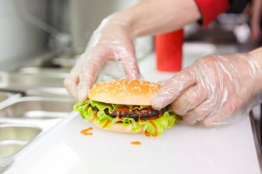 Aşçı hamburgerin ikinci yarısını ekliyor. Restoranda hamburger hazırlıyorum. Aşçının elleri hijyen şartlarına göre tek kullanımlık eldivenlerle..