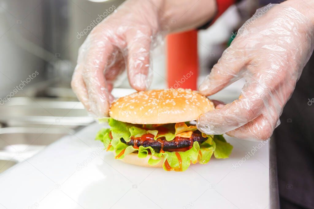 The chef's hands demonstrate the finished Burger. Preparing burger in restaurant. Hands of the cook in disposable gloves based on hygiene requirements.
