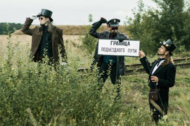 Steampunk takım elbiseli üç adam terk edilmiş bir demiryolunun yanında poz veriyor.