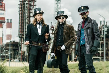 Steampunk tarzı üç adam endüstriyel arka planda duruyor.