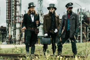 Steampunk tarzı üç adam endüstriyel arka planda duruyor.