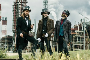Steampunk tarzı üç adam endüstriyel arka planda duruyor.
