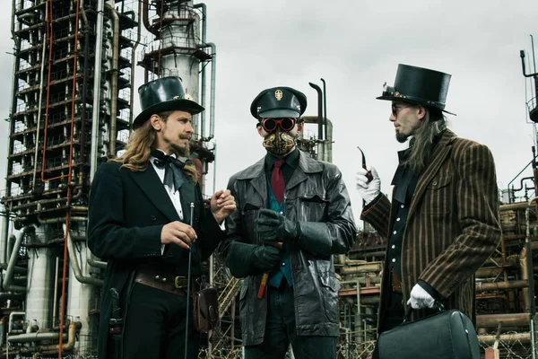 Three mans in steampunk style discuss standing against the industrial background
