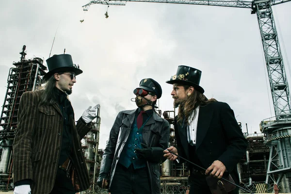 Τρεις Άνδρες Στυλ Steampunk Συζητούν Στέκεται Ενάντια Στο Βιομηχανικό Υπόβαθρο — Φωτογραφία Αρχείου