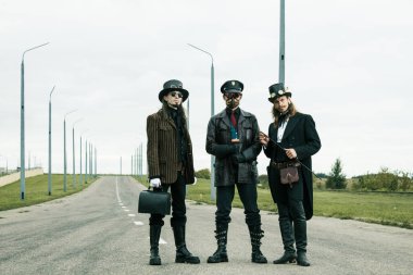 Steampunk tarzı üç adam yolda poz veriyor.