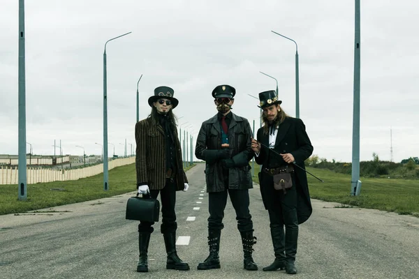 Steampunk tarzı üç adam yolda poz veriyor.