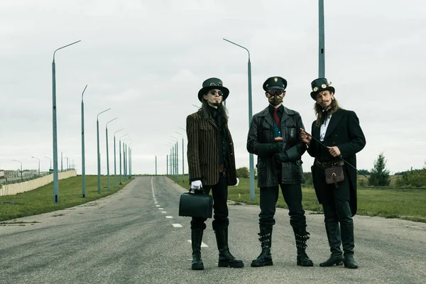 Steampunk tarzı üç adam yolda poz veriyor.