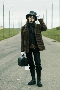 Steampunk tarzı giyinmiş genç adam yolda poz veriyor.