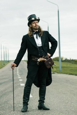 Steampunk tarzı giyinmiş genç adam yolda poz veriyor.
