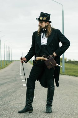 Steampunk tarzı giyinmiş genç adam yolda poz veriyor.