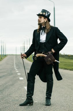Steampunk tarzı giyinmiş genç adam yolda poz veriyor.