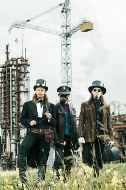 Steampunk tarzı üç adam endüstriyel arka planda duruyor.