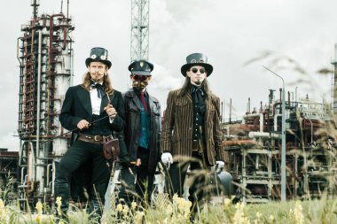 Steampunk tarzı üç adam endüstriyel arka planda duruyor.