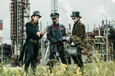 Steampunk tarzı üç adam endüstriyel arka planda duruyor.