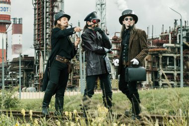 Steampunk tarzı üç adam endüstriyel arka planda duruyor.