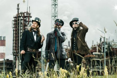 Steampunk tarzı üç adam endüstriyel arka planda duruyor.