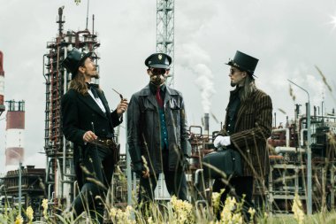 Steampunk tarzı üç adam endüstriyel arka planda duruyor.