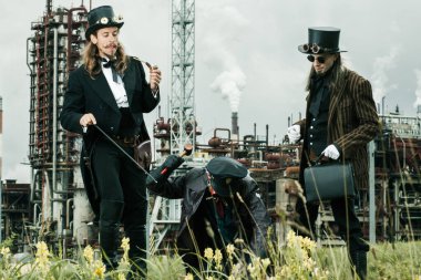 Steampunk tarzı üç adam endüstriyel arka planda duruyor.