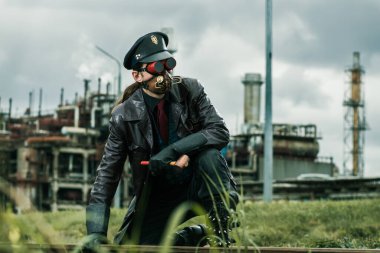 Çekiçli genç adam Steampunk tarzında giyinmiş fabrikanın yanındaki demiryolunda çalışıyor.