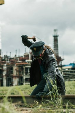 Çekiçli genç adam Steampunk tarzında giyinmiş fabrikanın yanındaki demiryolunda çalışıyor.