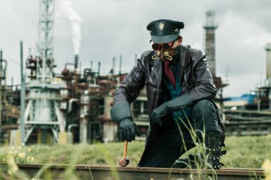 Çekiçli genç adam Steampunk tarzında giyinmiş fabrikanın yanındaki demiryolunda çalışıyor.