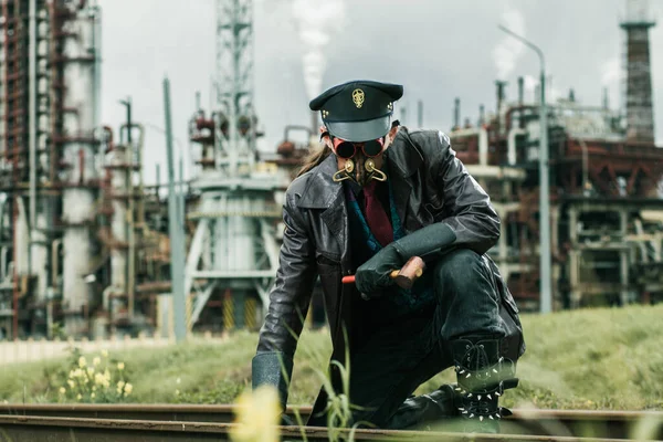 Young man with hammer weared in steampunk style working on railway near by factory