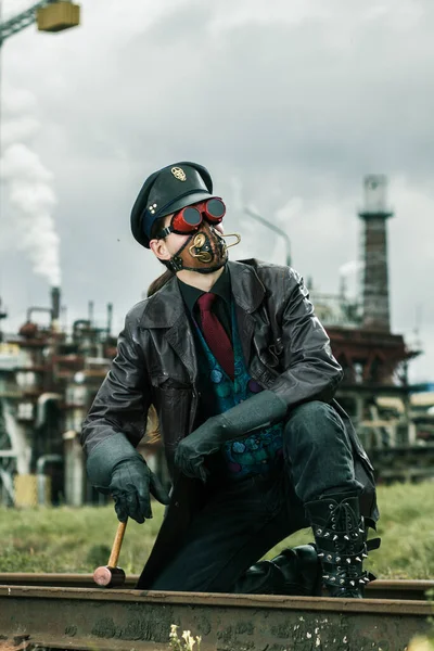 Young man with hammer weared in steampunk style working on railway near by factory