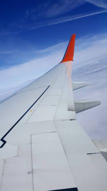 Bir uçak kanadında uçan bir uçağın penceresinden bak. Arka planda bulutlar ve mavi gökyüzü var.