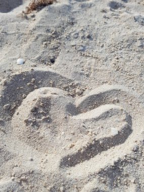 Bir kalp, ince, gri kumun üzerine dikkatsizce çizilmiştir.