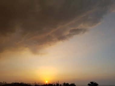 Uzakta bir sahil kasabasının silueti. Valer altından gri-turuncu renge gökyüzü ve bulutlar.