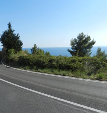 Asfalt yol, yeşillik ve açık deniz manzarası ve gökyüzünün sonsuz maviliği.