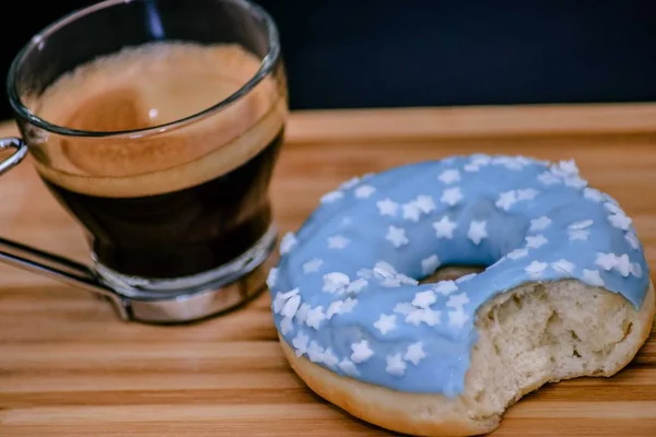 Close up of expresso coffee with a blue frosted bitten doughnut on bamboo surface — Stock Photo, Image