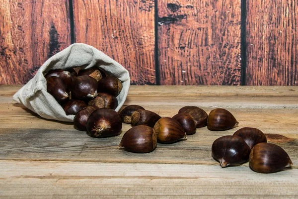 Castanhas caindo de um saco de tecido com um fundo de madeira — Fotografia de Stock