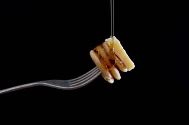 Üzerinde şerbet olan, siyah bir zemin üzerine izole edilmiş tereyağlı mini mısır gevreği krepleri tutan çatal.