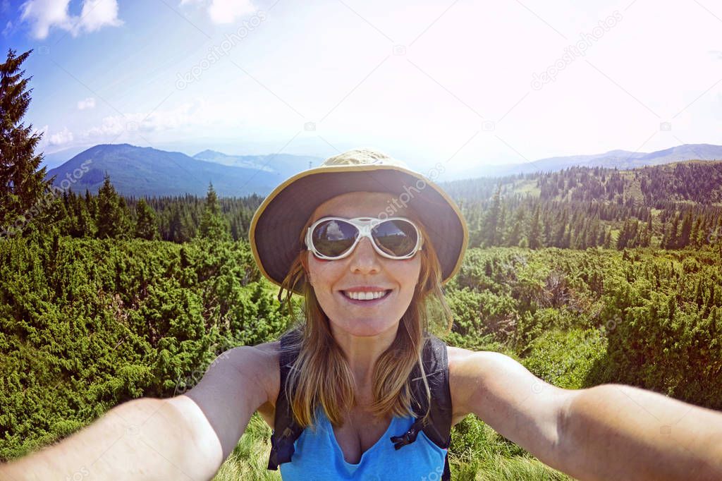 Smiling young woman takes a selfie  on mountain peak in Carpathian Mountains