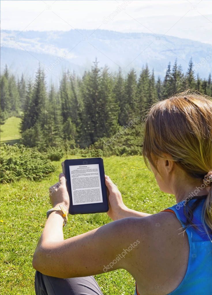 Close-up of woman reading e-book in nature. Girl holding tablet computer screen which is editable isolated on forest background  in Dragobrat ,Carpathian mountains ,Ukraine