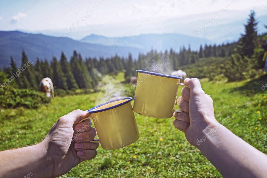 Young couple with cup of tea while looking on  forest on background of sunny mountains grass and hills  in Carpathian ,Dragobrat ,Ukraine 