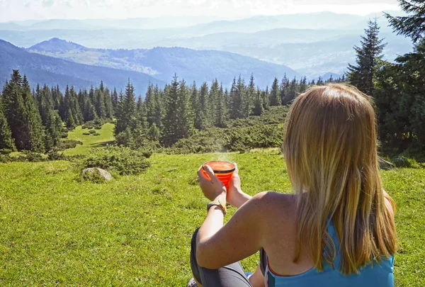 コーヒー 日当たりの良い山草やカルパチア Dragobrat ウクライナの丘の背景に林を見ながら 草の上に座ってのカップを持つ若い女性 — ストック写真