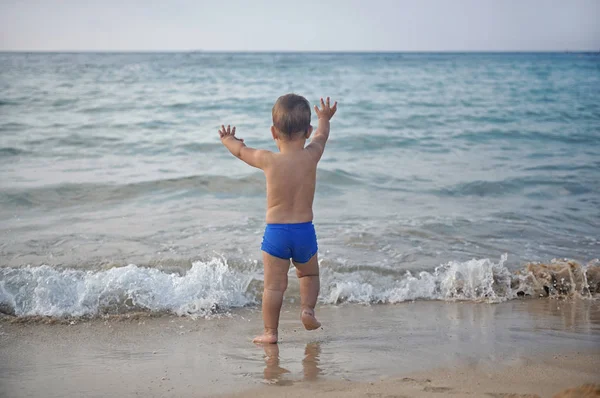 เด็กชายตัวเล็กวิ่งไปที่ทะเลสาบชายหาดมหาสมุทรตอนเย็นพระอาทิตย์ตกมองไกล . รูปภาพสต็อก