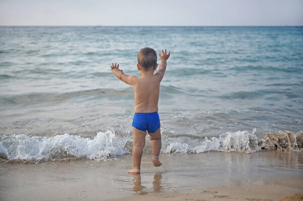 Small child  kid boy running to the sea lake ocean beach at evening sunset looking far away. Royalty Free Stock Photos