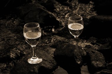 Akan suyun içinde taşlar üzerinde beyaz şarap bardakları